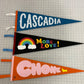 Three pennant flags in a row a blue one saying "Cascadia", a black one saying "More Love!", and an orange one saying "Chonk" 