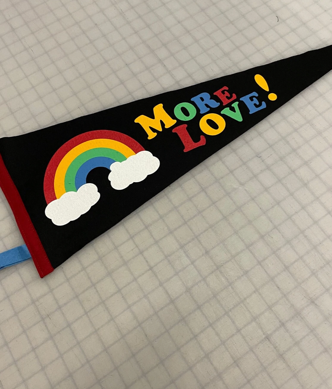 Black pennant flag with a rainbow that says "More Love!" in rainbow letters.