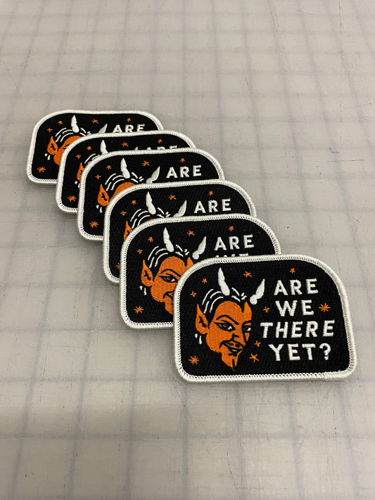 Black patch with a white edge with an orange devil that says  "Are we there yet?" in white letters