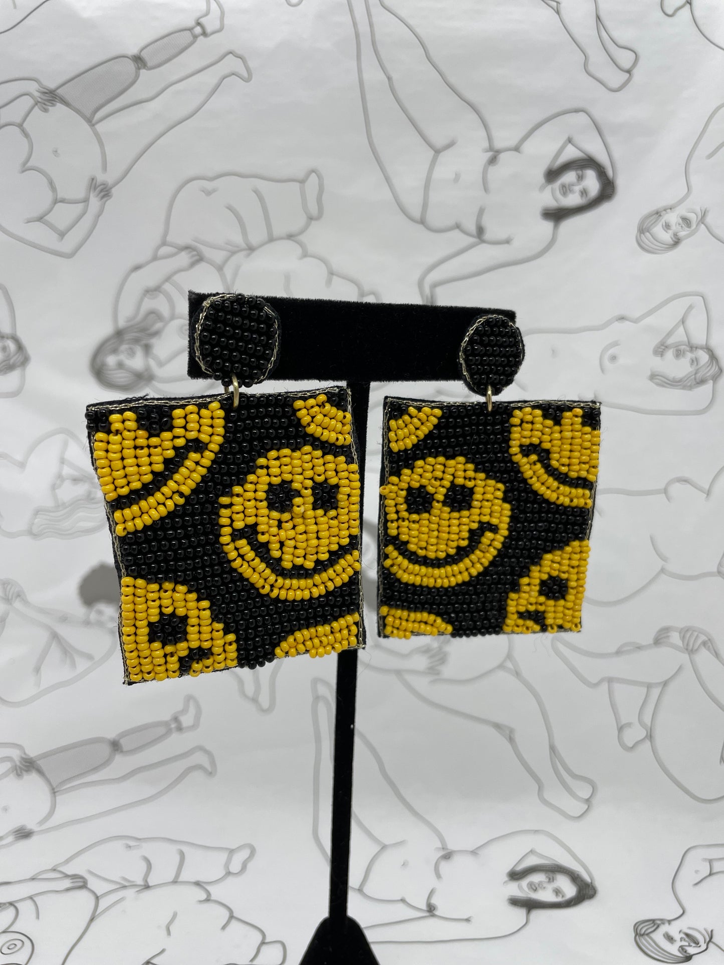 Post earrings with a dangly black beaded square with yellow beaded smily faces all over.
