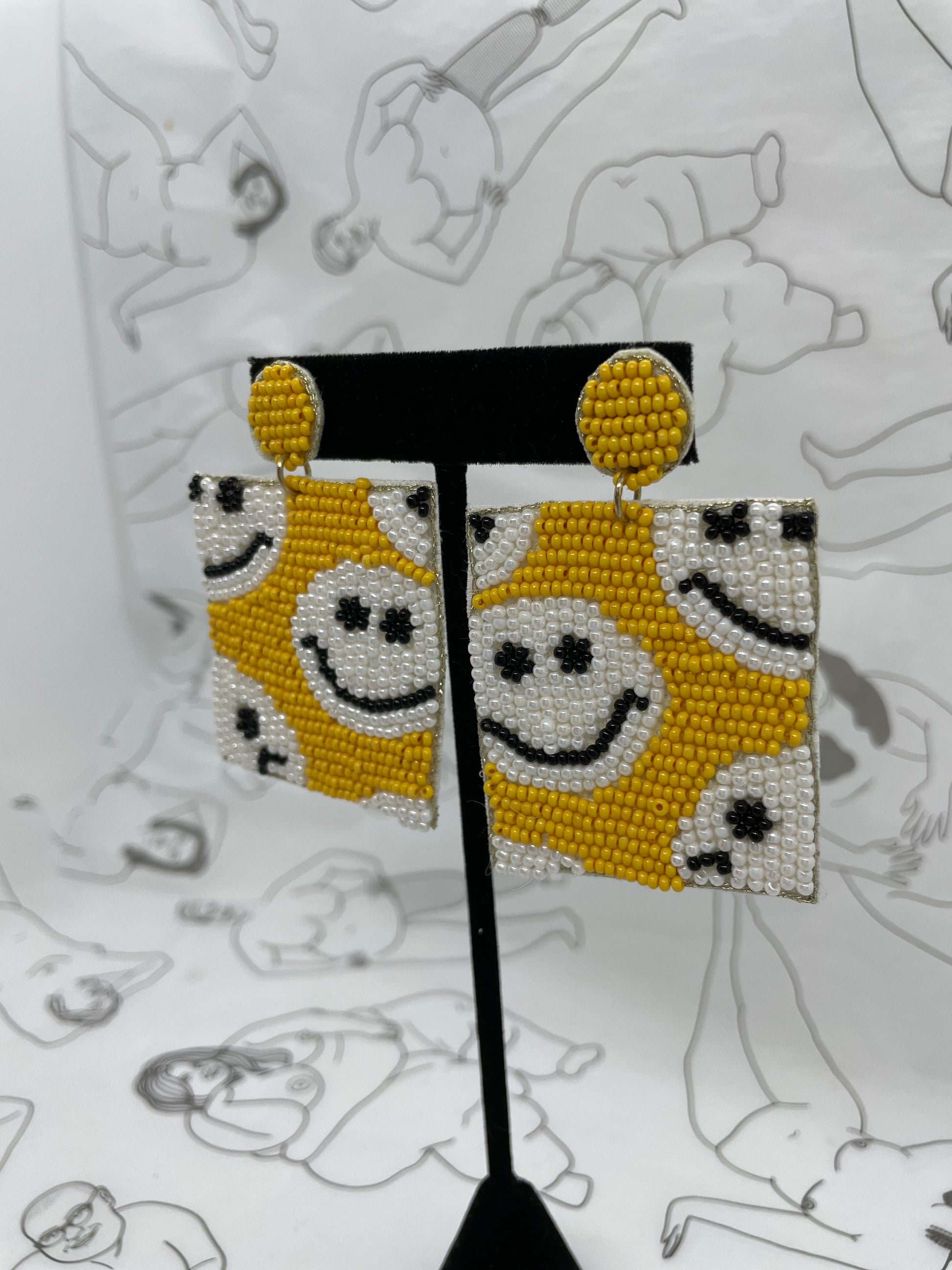 Post earrings with a dangly yellow beaded square with white beaded smily faces all over.