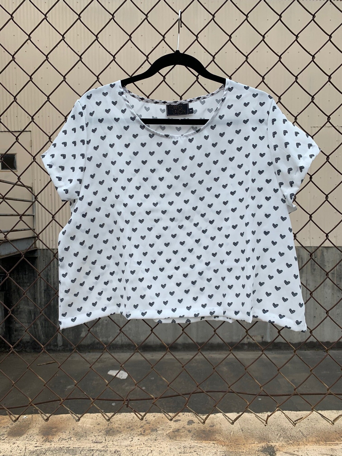 White scoop neck crop top with short sleeves and all over black heart pattern.