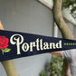 Navy blue pennant flag with a red rose that says "Portland" white in scrawled font and "Oregon" in small green letters.