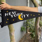 Black pennant flag with yellow stars that says "New York City" in white letters with the C as a yellow crescent moon
