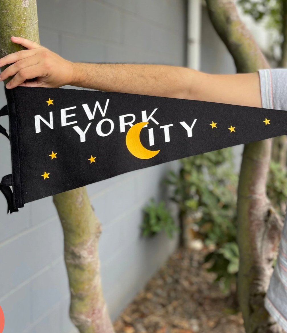 Black pennant flag with yellow stars that says "New York City" in white letters with the C as a yellow crescent moon