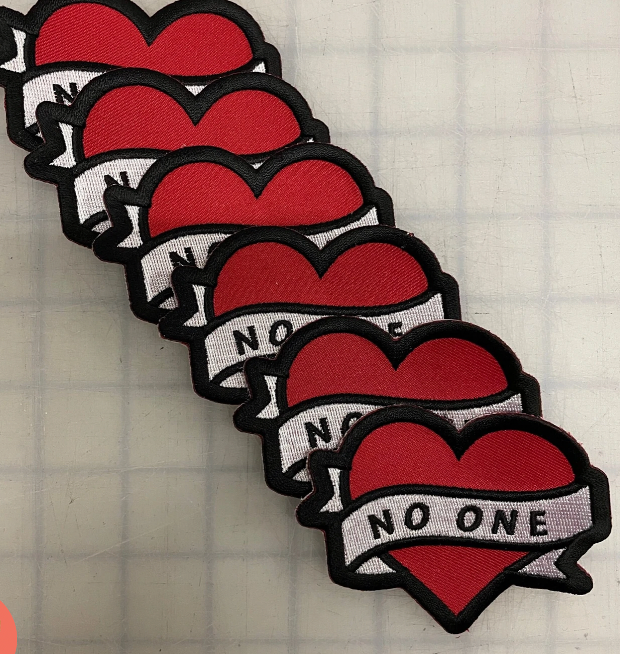 Red heart patch with a white banner across the heart that says "No one" in black letters