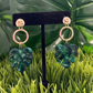 Gold post circle earrings with marbled green monsteras hanging from them.