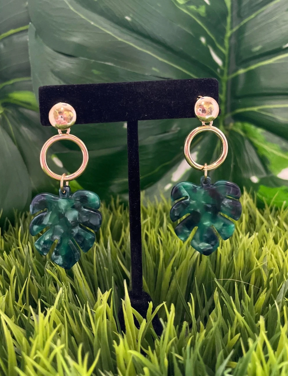 Gold post circle earrings with marbled green monsteras hanging from them.