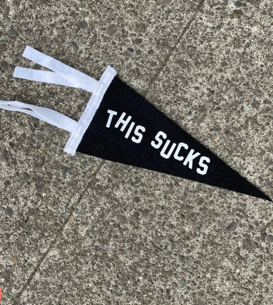 Black pennant flag that says "This Sucks" in uneven white letters.