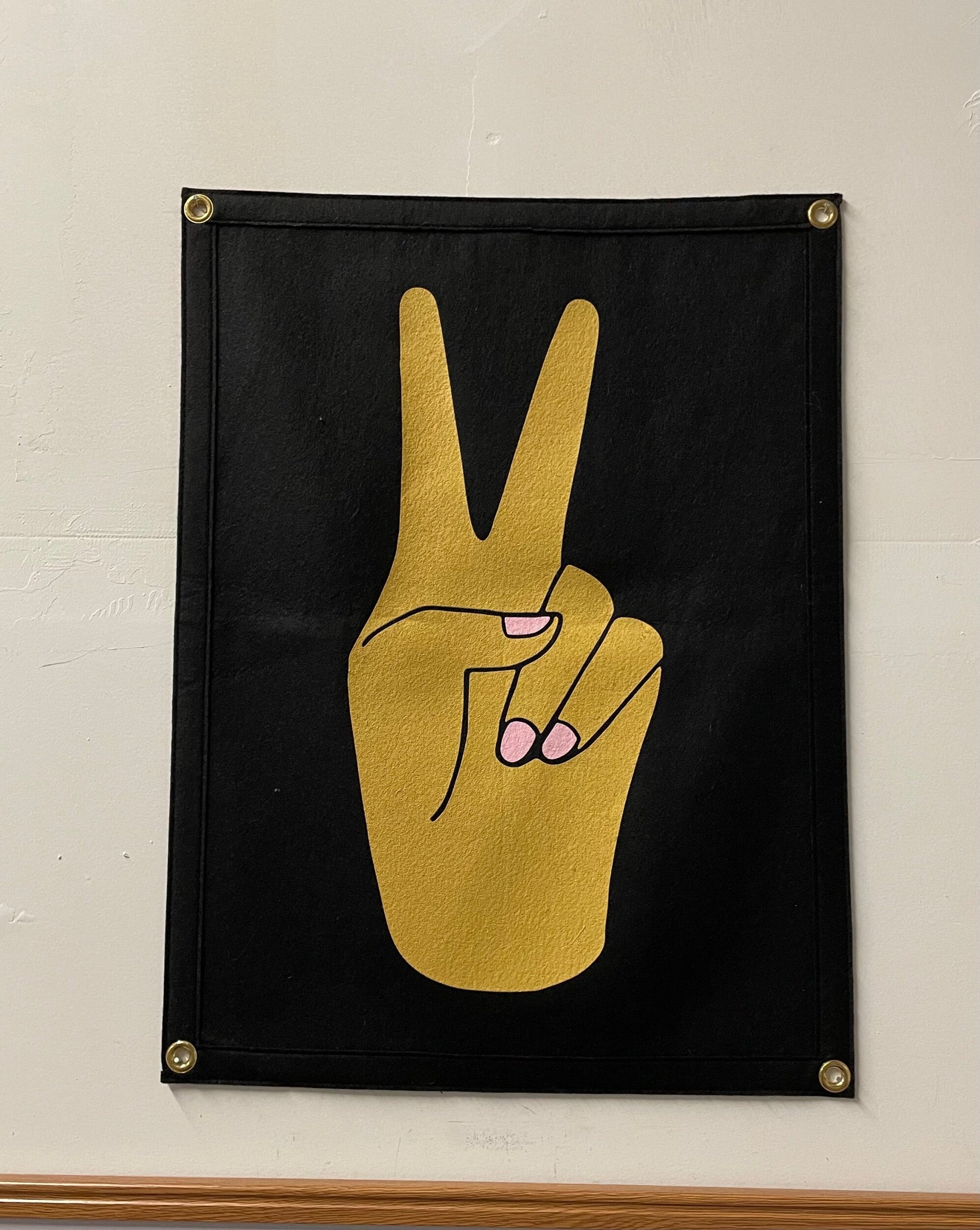 A black banner with a gold hand making a peace sign with pink nails.